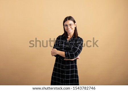A young woman in a plaid dress stands on an orange background and shows different emotions