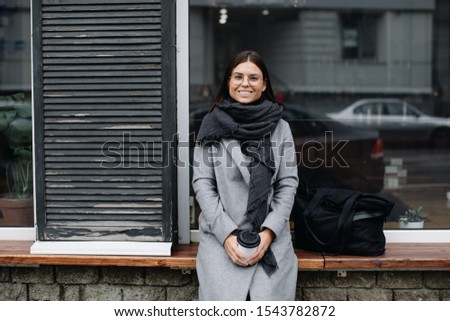 Portrait of a young woman in glasses. A young business woman stands at the window of a cafe and drinks coffee