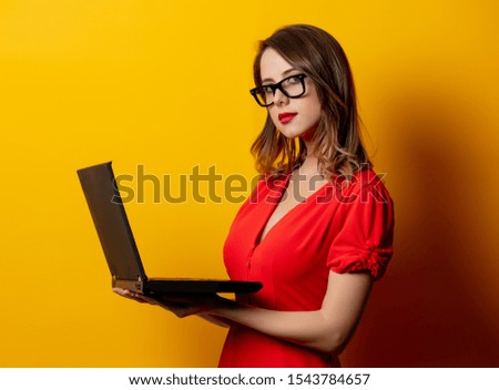 Beautiful woman in red dress with laptop computer on yellow background