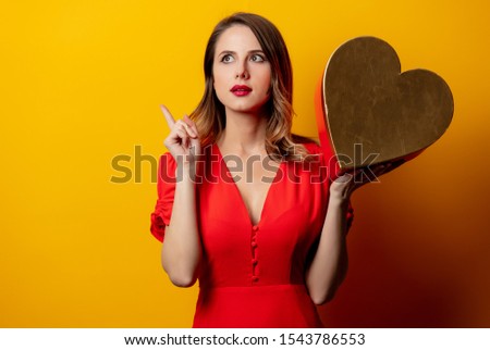 Beautiful woman with heart shape box on yellow background 