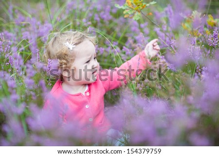 Cute happy baby girl playing with beautiful purple flowers in a heather landscape in Holland