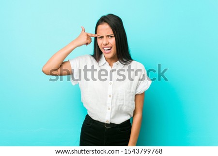 Young hispanic cool woman against a blue wall showing a disappointment gesture with forefinger.