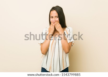 Young hispanic woman laughing about something, covering mouth with hands.