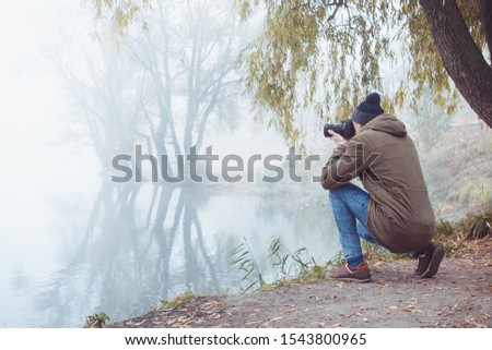 A young man with a camera takes pictures of autumnal nature while traveling.