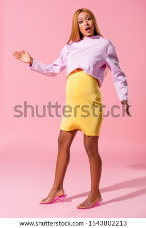pregnant, shocked african american woman looking at camera on pink background, fashion doll concept