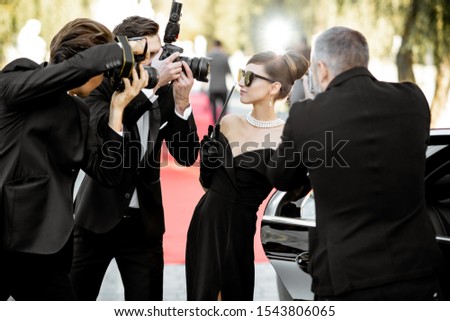 Beautiful woman dressed in retro style as a famous movie actress arriving on the awards ceremony with annoying photo reporters taking pictures of her