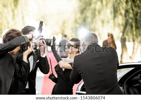 Beautiful woman dressed in retro style as a famous movie actress arriving on the awards ceremony with annoying photo reporters taking pictures of her