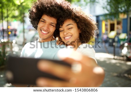 Portrait of happy afro couple taking selfie outside in city