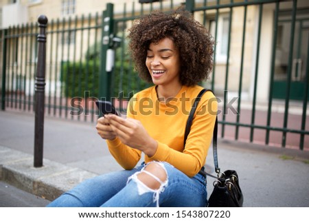 Portrait of smiling african american young woman looking at cellphone in city