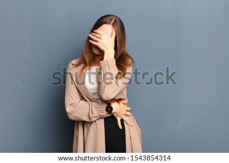 young pretty woman looking stressed, ashamed or upset, with a headache, covering face with hand against gray background Royalty-Free Stock Photo #1543854314