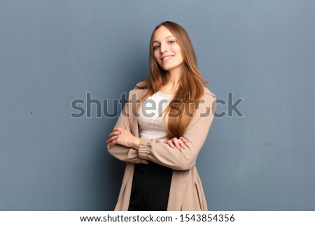 young pretty woman smiling to camera with crossed arms and a happy, confident, satisfied expression, lateral view against gray background Royalty-Free Stock Photo #1543854356