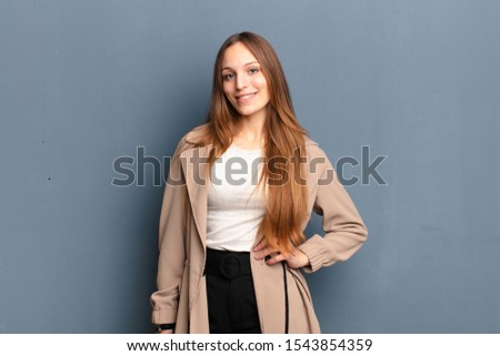 young pretty woman smiling happily with a hand on hip and confident, positive, proud and friendly attitude against gray background Royalty-Free Stock Photo #1543854359