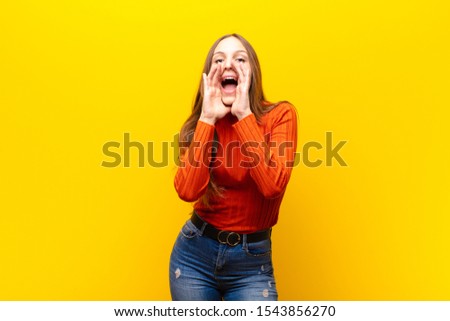 young pretty woman feeling happy, excited and positive, giving a big shout out with hands next to mouth, calling out against orange background Royalty-Free Stock Photo #1543856270