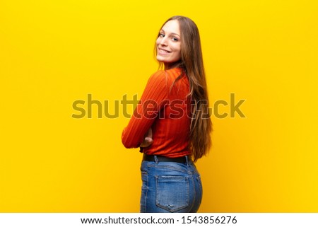young pretty woman smiling gleefully, feeling happy, satisfied and relaxed, with crossed arms and looking to the side against orange background Royalty-Free Stock Photo #1543856276