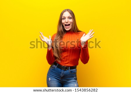 young pretty woman feeling happy, excited, surprised or shocked, smiling and astonished at something unbelievable against orange background Royalty-Free Stock Photo #1543856282