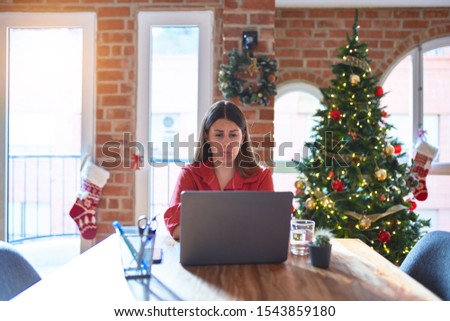Beautiful woman sitting at the table working with laptop at home around christmas tree depressed and worry for distress, crying angry and afraid. Sad expression.