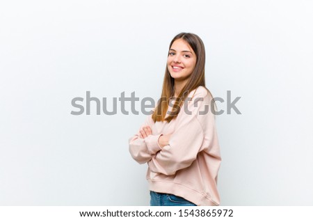 young pretty woman smiling to camera with crossed arms and a happy, confident, satisfied expression, lateral view against white background Royalty-Free Stock Photo #1543865972