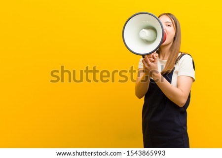 young pretty woman  with a megaphone against orange background Royalty-Free Stock Photo #1543865993