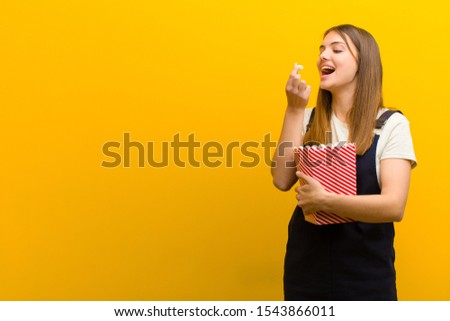 young pretty woman with  pop corns  against orange background Royalty-Free Stock Photo #1543866011