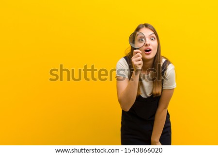 young pretty woman  with a magnifying glass against orange background Royalty-Free Stock Photo #1543866020