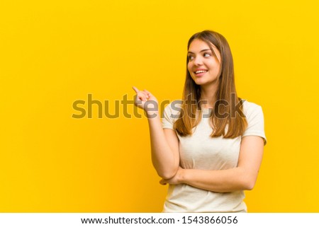 young pretty woman smiling happily and looking sideways, wondering, thinking or having an idea against orange background Royalty-Free Stock Photo #1543866056