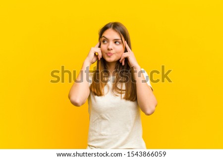young pretty woman feeling confused or doubting, concentrating on an idea, thinking hard, looking to copy space on side against orange background Royalty-Free Stock Photo #1543866059