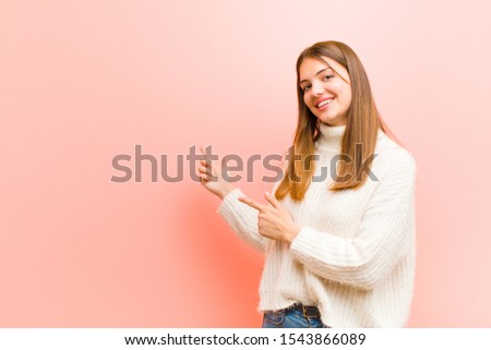 young pretty woman smiling happily and pointing to side and upwards with both hands showing object in copy space against pink background Royalty-Free Stock Photo #1543866089