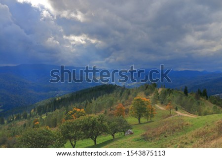 The photo was taken in Ukraine, in the Carpathian mountains. In the picture, a ray of sun breaking through thunderclouds and illuminating the autumn landscape of mountains.