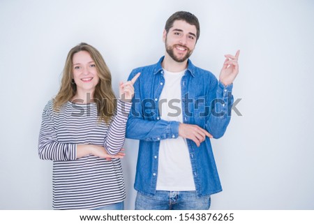 Young beautiful couple standing together over white isolated background with a big smile on face, pointing with hand and finger to the side looking at the camera.