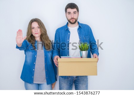 Young couple holding cardboard box moving to new house over white isolated background with open hand doing stop sign with serious and confident expression, defense gesture