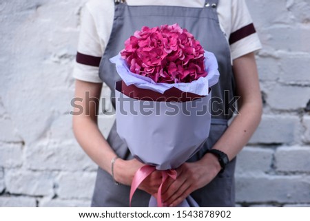 Bouquet of pink hydrangea in the package in woman's hands on a light background