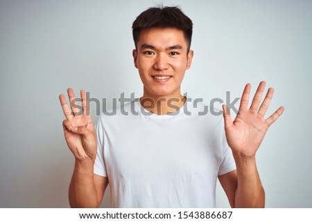 Young asian chinese man wearing t-shirt standing over isolated white background showing and pointing up with fingers number eight while smiling confident and happy.