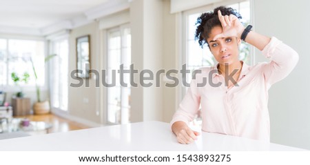 Wide angle of beautiful african american woman with afro hair making fun of people with fingers on forehead doing loser gesture mocking and insulting.