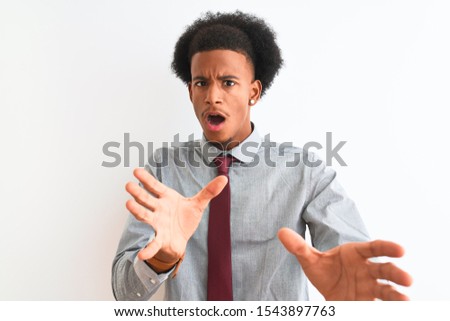 Young african american businessman wearing tie standing over isolated white background afraid and terrified with fear expression stop gesture with hands, shouting in shock. Panic concept.