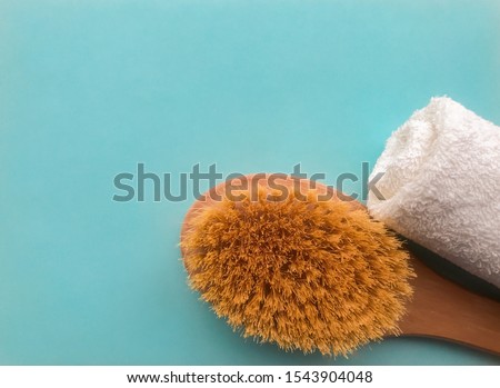 Brush for the body and white towel rolled in a roll  on a turquoise background with place for text. The concept of the SPA, cleansing the body, anti-cellulite