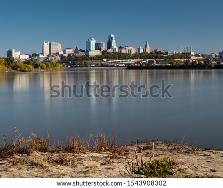 Downtown Kansas City skyline reflecting in Missouri River with blue sky.