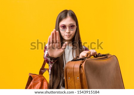 Young asian woman holding a suitcase standing with outstretched hand showing stop sign, preventing you.
