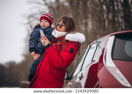 Mother with son standing by car in winter and talking on phone
