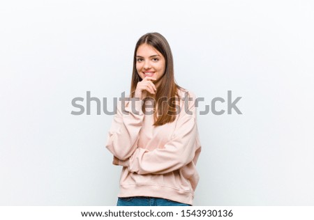 young pretty woman looking happy and smiling with hand on chin, wondering or asking a question, comparing options against white background Royalty-Free Stock Photo #1543930136