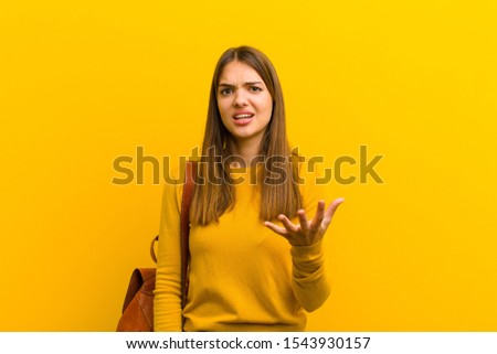young pretty woman looking angry, annoyed and frustrated screaming wtf or what‚Äôs wrong with you against orange background Royalty-Free Stock Photo #1543930157