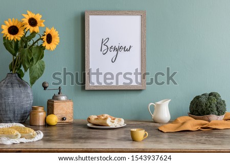 Stylish and elegant home interior of kitchen space with wooden mock up poster frame, sunflowers in vase, fresh vegetables and kitchen accessories. Nice home decor. Template. Eucalyptus color concept.