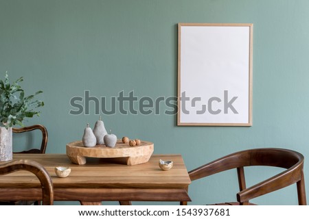 Stylish scandinavian dining room interior with mock up poster frame, wooden table, furniture, cup of coffee, plant , cement fruits, nuts and elegant accessories.  Template. Modern home decor.