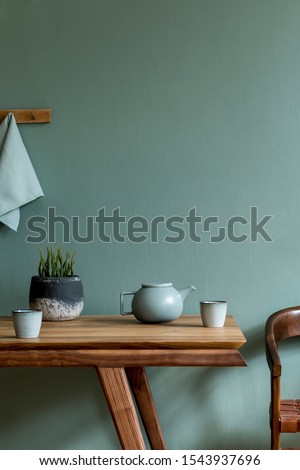 Stylish and minimalistic dining room interior with wooden table, teapot with cups, plant and elegant accessories. Eucalyptus color. Ready to use. Template. Modern home decor. Copy space.
