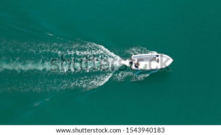 Aerial drone bird's eye top view photo of small motor boat cruising in emerald clear water lake