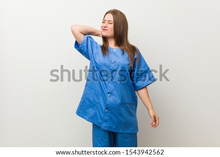 Young nurse woman against a white wall suffering neck pain due to sedentary lifestyle.