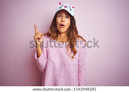 Young beautiful woman wearing funny cat cap standing over pink isolated background pointing finger up with successful idea. Exited and happy. Number one.