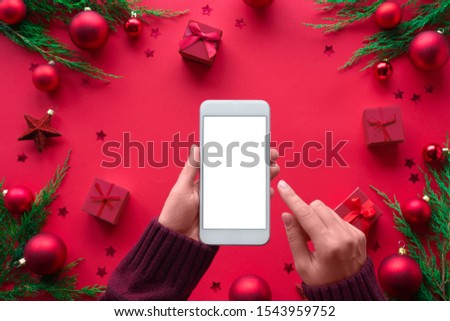 Female hand hold phone on merry christmas red background, girl customer shopper using online mobile shopping app choosing holiday gifts with mobile payments on mock up white screen, close up top view Royalty-Free Stock Photo #1543959752