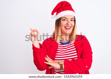 Young beautiful woman wearing Christmas Santa hat over isolated white background with a big smile on face, pointing with hand and finger to the side looking at the camera.