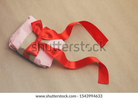 Soft pouch wrapped in craft paper and tie red satin ribbon. Crumpled paper background texture. Delivery service. Online shopping.	

