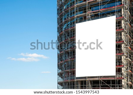 Blank white banner for advertisement hanging on the scaffolding of modern building under construction